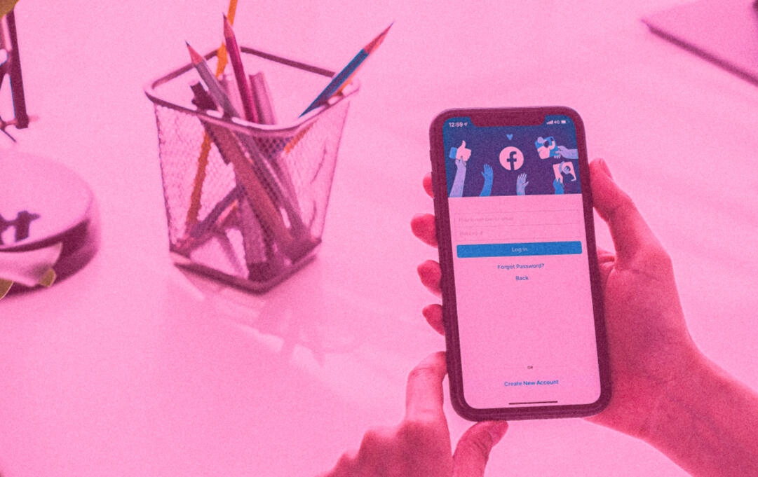 person's hands holding a smart phone at a desk, with Facebook social media site login window
