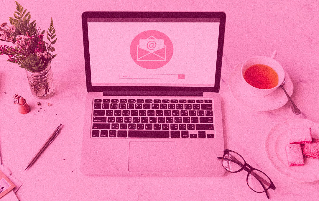 a laptop with an email icon on the screen, along with glasses, tea, glowers, and snacks on a desk